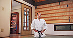 Martial arts, kneeling and Japanese man with respect, honor and karate etiquette in dojo. Japan, combat training and fight studio with sport, discipline and warrior in taekwondo class in gym