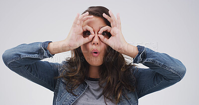 Buy stock photo Binocular, fingers and silly woman with playful expression or gesture in studio for vision or funny face. Female person, comic hand glasses and white background for joke, sign and wow perspective