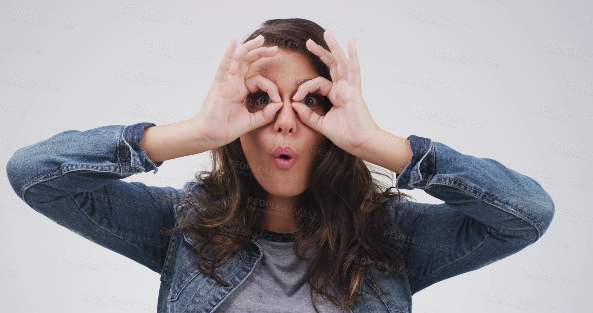 Buy stock photo Binocular, fingers and silly woman with playful expression or gesture in studio for vision or funny face. Female person, comic hand glasses and white background for joke, sign and wow perspective