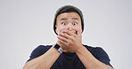 Scared, shocked and portrait of man in studio with omg, wtf or wow reaction for news. Emotion, surprise and Asian male person with hands covering mouth for rumor or announcement by white background.
