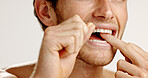 Dental care, floss and man in studio with hygiene, wellness and mouth routine in morning. Oral health, fresh breath and person with string for cleaning teeth with plaque removal by white background.