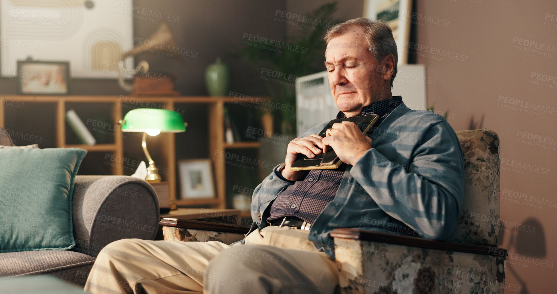 Buy stock photo Senior, sad man and hug with photo frame for memory, grief or loss in regret on chair at home. Elderly, male person or thinking with picture, depression or nostalgia for missing piece or lonely house