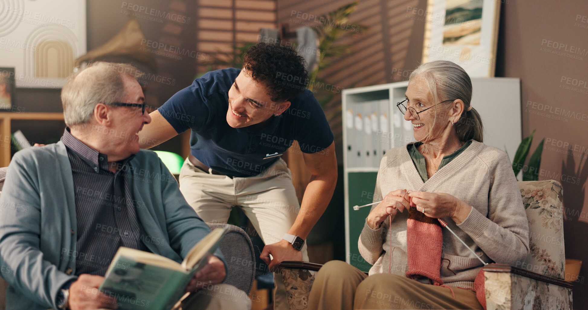 Buy stock photo Living room, caregiver and talk with old couple, hobby and senior people with smile in nursing home. Knitting, elderly woman and man with book in lounge, nurse and conversation with patient in house