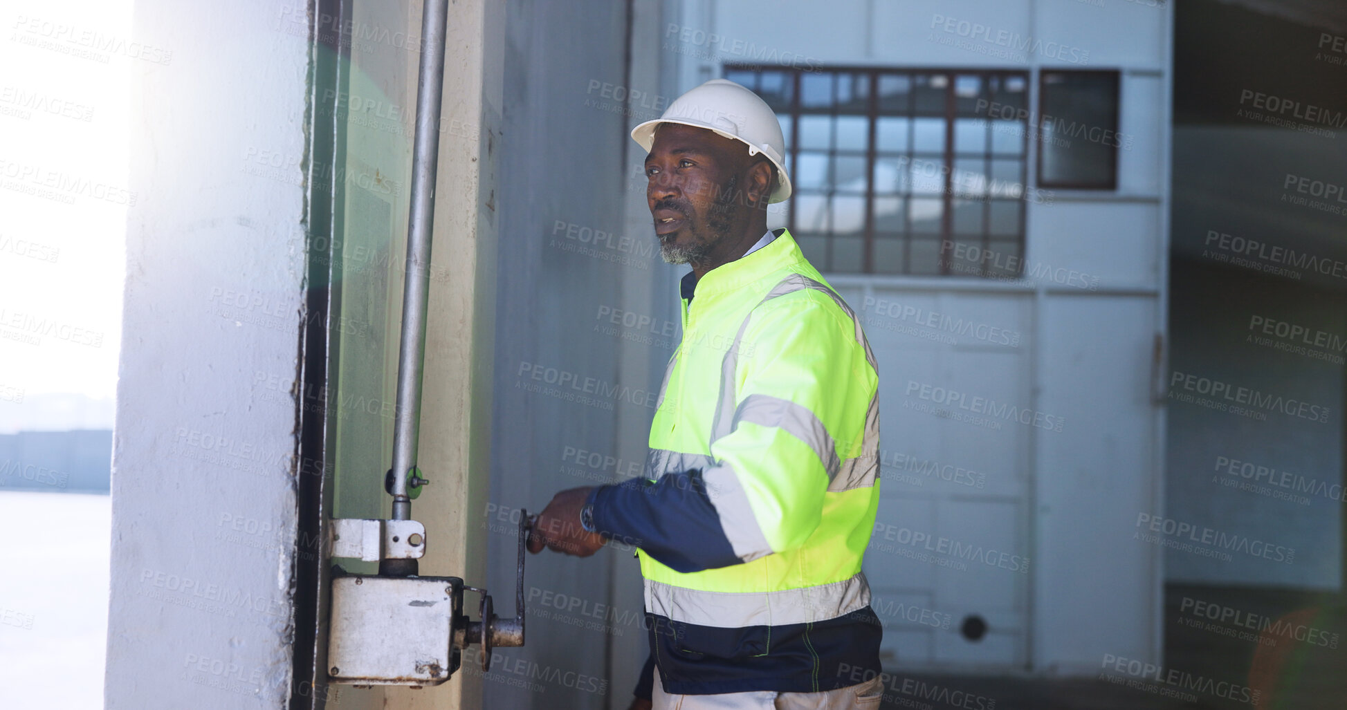 Buy stock photo Mature man, garage door and open for shipping, stock or storage at warehouse for supply chain. African person, engineer and maintenance for gate, check or commercial distribution at industrial plant