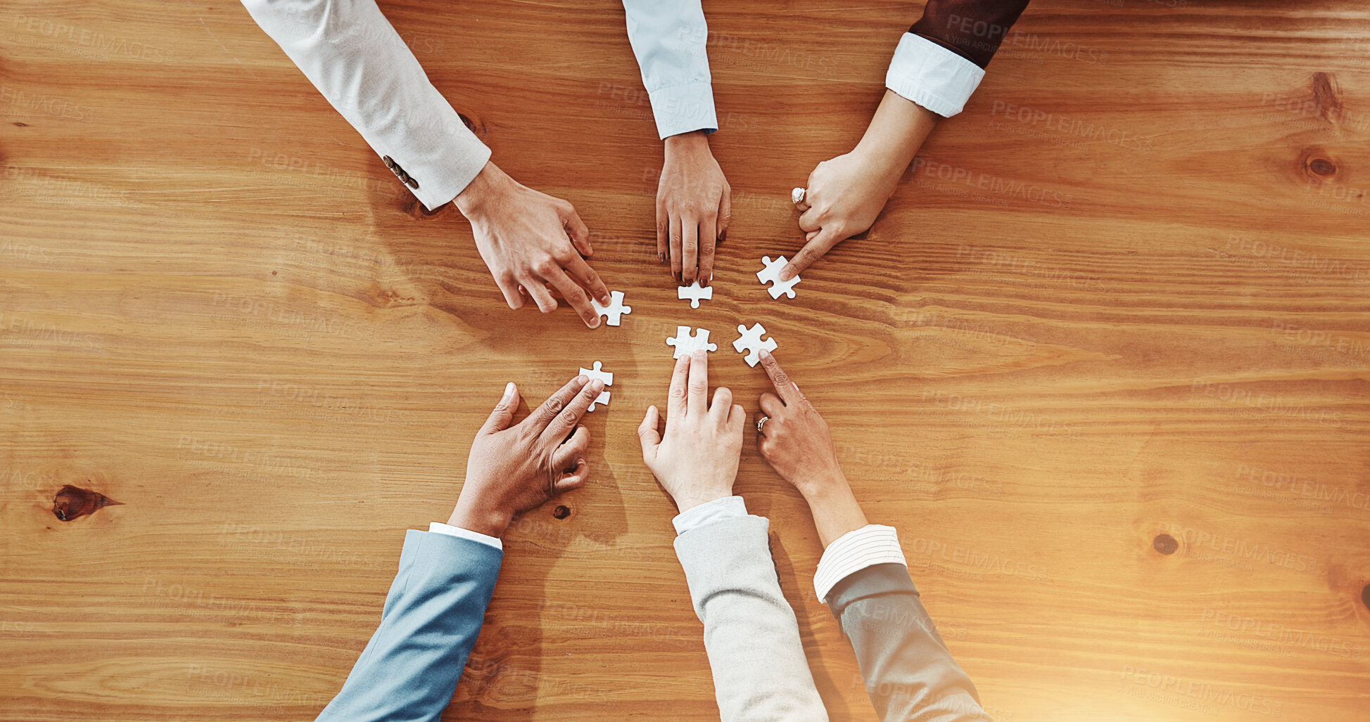 Buy stock photo Business people, hands and meeting with jigsaw puzzle for team building on wooden table above. Top view, group or employees with pieces for unity, problem solving or collaboration together on space