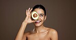 Skincare, happy and woman with avocado in studio for hydration, natural antioxidants and vitamin c. Mockup, beauty and girl with fruit for skin elasticity and anti aging benefits on brown background