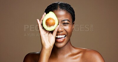 Buy stock photo Skincare, happy and black woman with avocado in studio with natural, antioxidants or face glow. Smile, beauty and African female person with fruit for moisturizing dermatology by brown background.