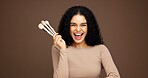 Beauty, happy and woman with makeup brushes in studio for concealer, skincare product and self care. Mockup, beautician and portrait with cosmetics tools on brown background for contour or foundation