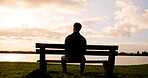 Man, thinking or back view with sunset on bench at lake for daydreaming, memory or break in nature. Male person, relax and fresh air with cloudy sky for rest, contemplating or travel at river or pond