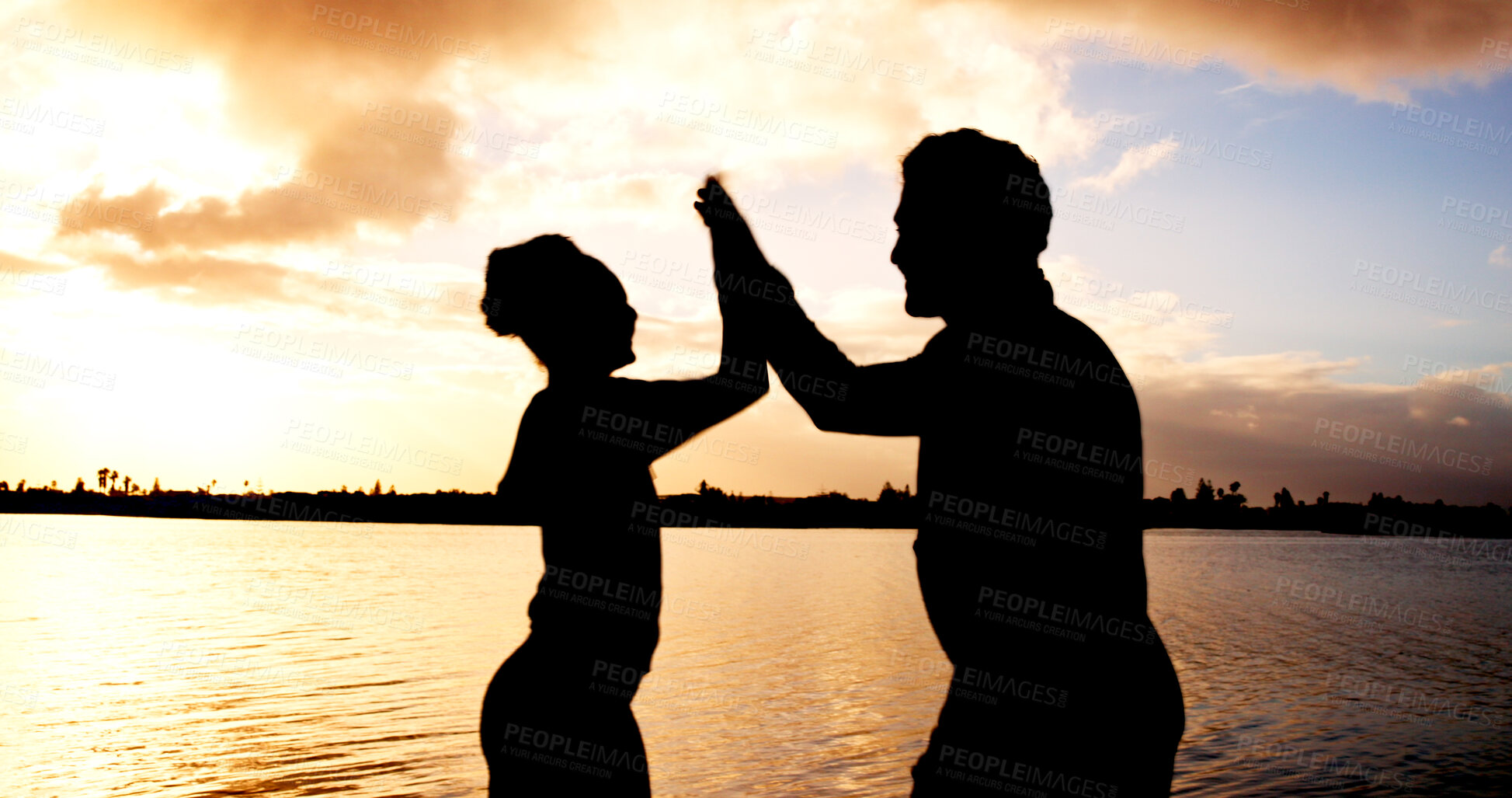 Buy stock photo Silhouette, couple and high five with sunset at river for winning, teamwork or success in nature. Active, man or woman with touch for evening activity, achievement or accomplishment together at lake