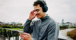 Headphones, fitness or man on bridge with phone for workout, tracking exercise or song. Lake, smile or athlete runner on mobile app in city for running progress, music playlist and podcast audio
