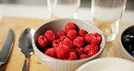 Health, home and bowl of raspberries on table for healthy eating, nutrition and wellness in kitchen. Closeup, food and fruit for organic snack, breakfast and meal for vitamins, benefits and diet