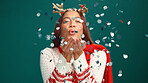 Confetti, Christmas and portrait of woman in studio for party, festive season and holiday. Happy, December and person with decoration, glitter and blowing for xmas celebration on green background