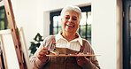 Senior woman, painter and portrait in home with artwork, tools and canvas for inspiration in retirement. Elderly person, artist and paint brush with hobby, smile or creative talent at house in Mexico