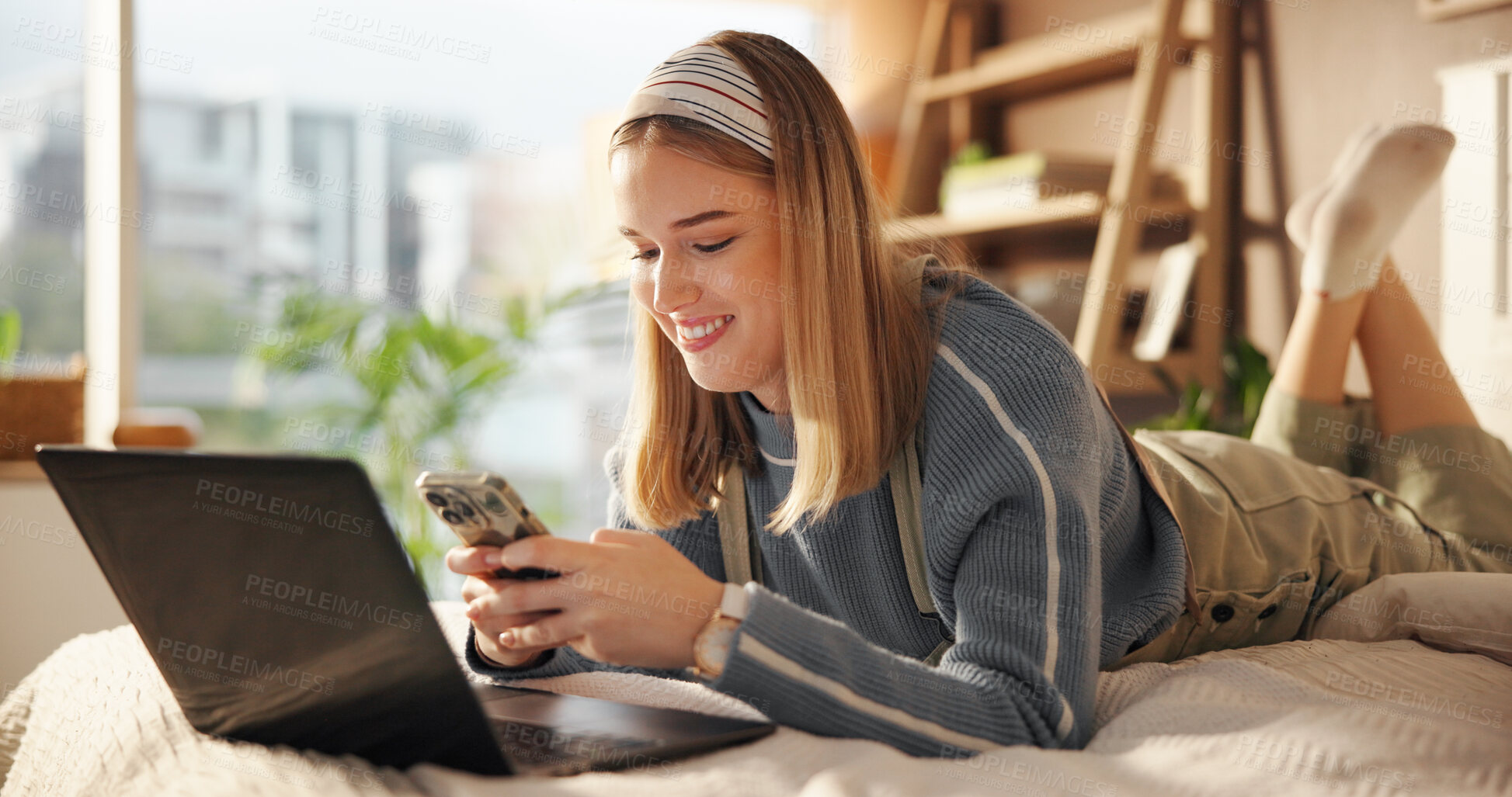 Buy stock photo Laptop, phone and relax with student in bedroom of home for college or university communication. App, computer and education with happy girl lying on bed to check class schedule for scholarship