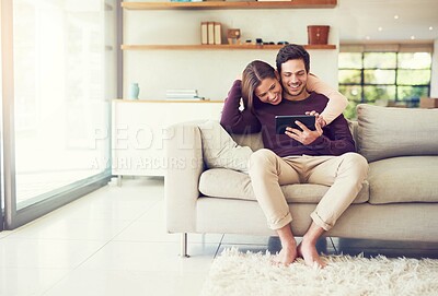 Buy stock photo Shot of a cheerful young couple using a digital tablet while relaxing on the sofa at home
