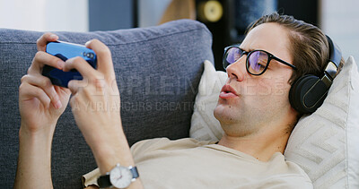 Buy stock photo Home, headphones and man on couch, cellphone and typing with video game, relax and audio. Apartment, comfort and person with smartphone, streaming service and listening to music and online platform