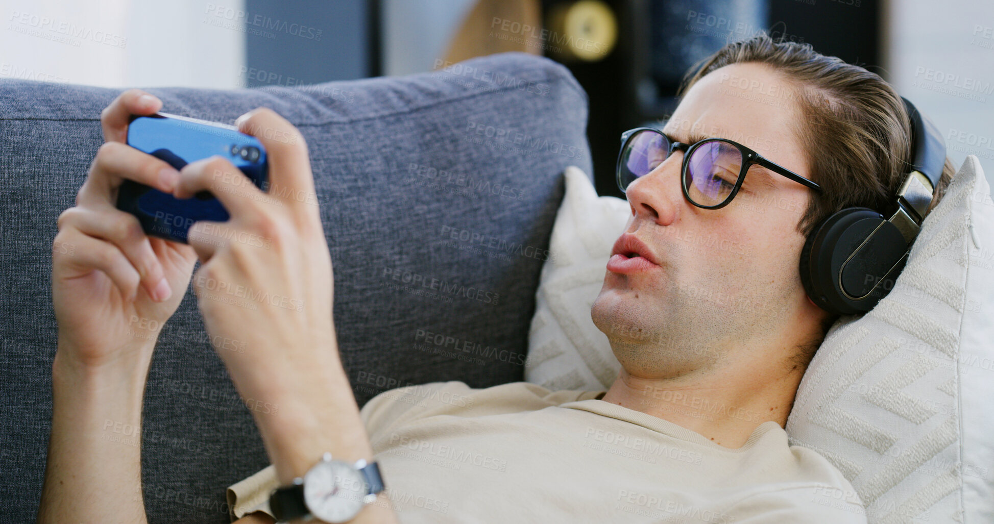 Buy stock photo Home, headphones and man on couch, cellphone and typing with video game, relax and audio. Apartment, comfort and person with smartphone, streaming service and listening to music and online platform