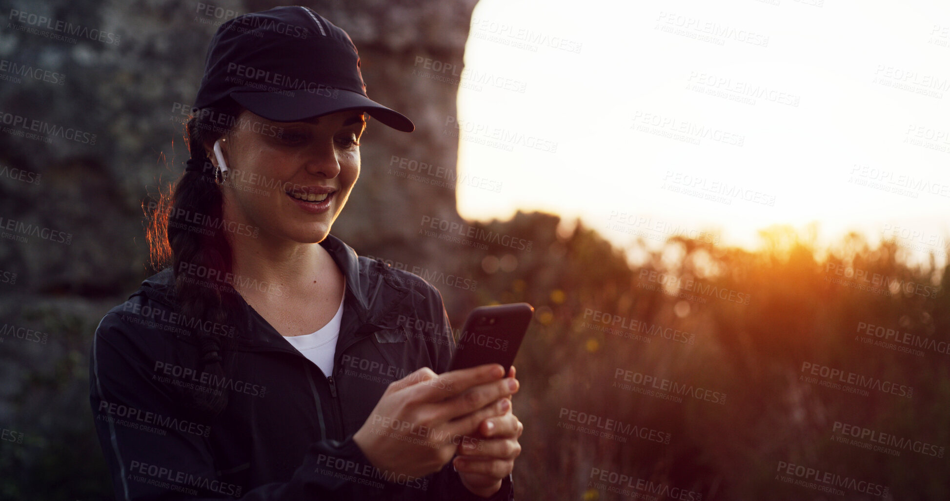 Buy stock photo Woman, athlete and music with smartphone, outdoor or listen to audio with earphones, smile or break. Fitness, happy and person with mobile for playlist, sunset and streaming with tech in nature