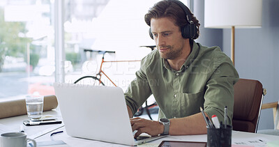 Buy stock photo Business, headphones and laptop with man in green office for streaming sound as startup employee. Computer, music and typing with designer person in eco friendly workplace for project management