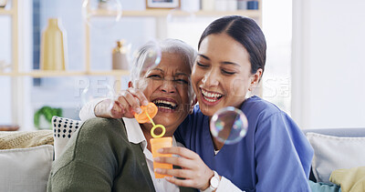 Buy stock photo Caregiver, old woman and blowing bubbles with laugh, medical support or happy in retirement home. Soap toy, nurse and elderly patient in living room for funny game with hug, bonding and healthcare