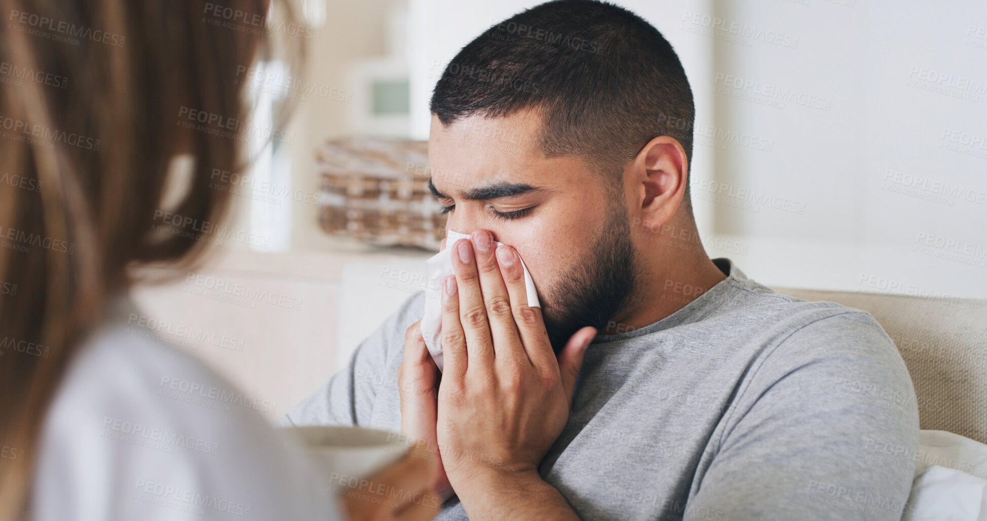 Buy stock photo Sick, man and blowing nose at house for allergies, virus problem and influenza symptoms. Ill, male person and tissue for sinus, woman helping and sneezing, viral infection and herbal tea for recovery