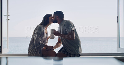 Buy stock photo Kiss, love and coffee with couple at window of home for connection, romance and peace. Relax, bonding and commitment with man and woman and drink tea in apartment for marriage, space and morning