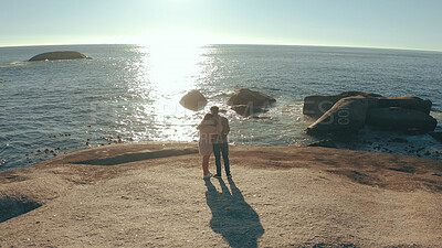 Buy stock photo Hug, love and back of couple by ocean for relaxing on holiday, vacation and weekend together. Dating, travel and man with woman embrace by sea, water and rocks for bonding, relationship or romance