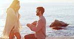 Man, woman and surprise with engagement ring at beach, kneeling and profile at sunset on vacation. Couple, question and jewelry with wow, commitment and marriage offer by ocean on holiday in Spain
