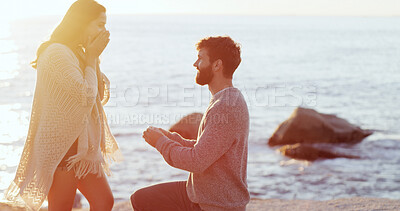 Buy stock photo Man, woman and surprise with engagement ring at beach, kneeling and profile at sunset on vacation. Couple, question and jewelry with wow, commitment and marriage offer by ocean on holiday in Spain