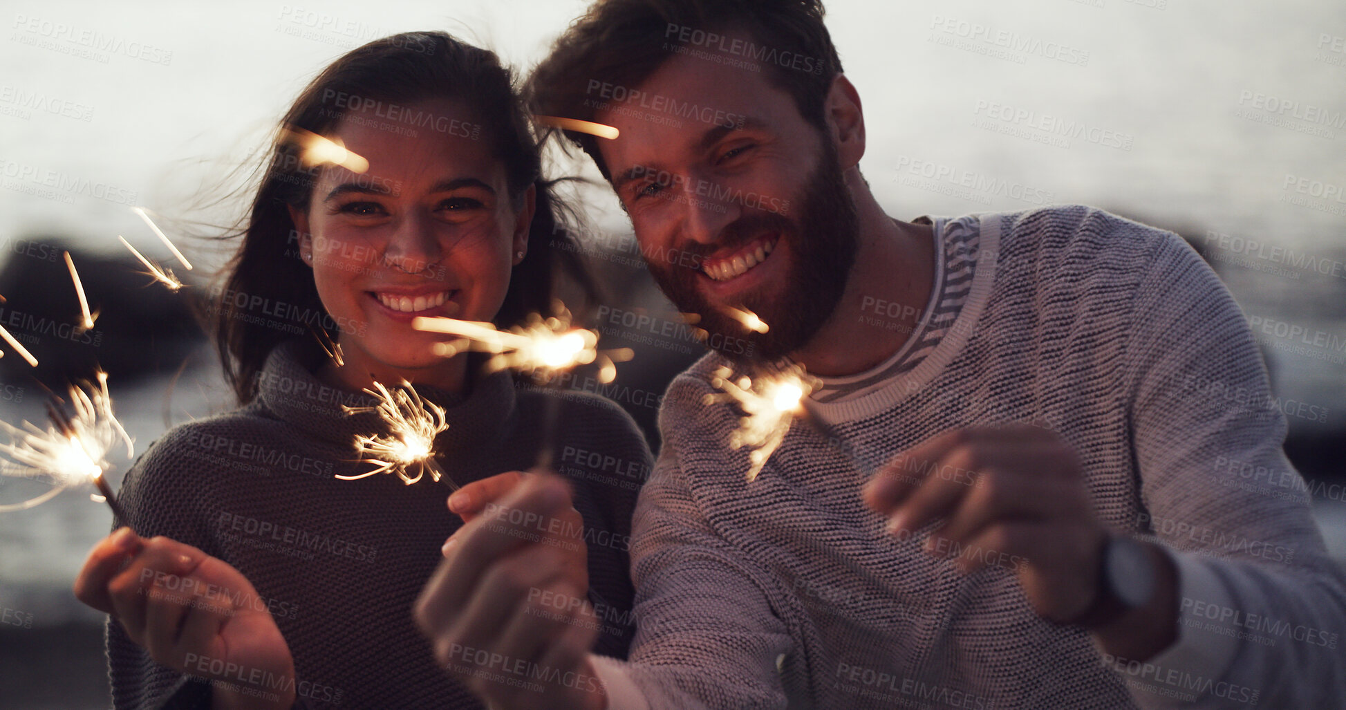 Buy stock photo Couple, sparkler and night at beach for celebration, bonding and love on relationship anniversary. People, fireworks and excited with portrait, party or holiday by ocean for new years eve in Spain