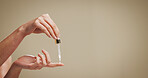 Beauty, serum and hands of person in studio for hyaluronic acid, skincare and anti aging. Mockup space, dermatology and finger with dropper for cosmetics, collagen and retinol on brown background
