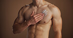 Hands, man or cream on body in studio for skin hydration, sunscreen protection or self care routine. Skincare, person or lotion application on chest for moisturizer or dermatology on brown background