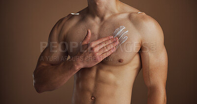 Buy stock photo Hands, man or cream on body in studio for skin hydration, sunscreen protection or self care routine. Skincare, person or lotion application on chest for moisturizer or dermatology on brown background