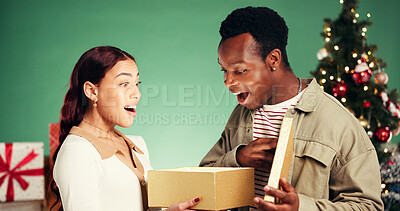 Buy stock photo Christmas, gift and shocked with interracial couple in studio for holiday season, celebration and xmas. Present, festive tradition and man with woman and box on green background for surprise and wow