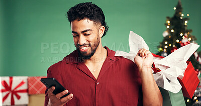 Buy stock photo Shopping bag, Christmas and man with smartphone, studio or discount for presents on December holiday. Ecommerce, purchase and person with gifts for Xmas, green background and browsing on mobile app