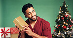 Man, Christmas and curious with surprise gift in studio, holiday and festive season on green background. Wonder, guess and male person with smile for present, celebration bokeh or xmas package