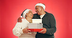 Christmas, hug and senior couple with gift, box and giving with retirement discount in studio. Love, happy man and woman together for marriage, present or festive holiday sale on red background space