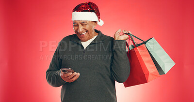 Buy stock photo Phone, shopping bags and senior man with christmas in studio with networking on mobile app. Laugh, gifts and elderly male person with cellphone for communication with xmas season by red background.