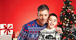 Christmas, portrait and happy people hug with child for love and holiday celebration. Man, son and embrace for xmas event with smile, festive season and family with support on red studio background