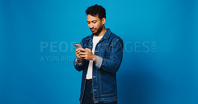 Buy stock photo Reading, phone and typing with man in studio for social media, communication and blog post. Online news feed, text message and networking chat with person on blue background for space and app