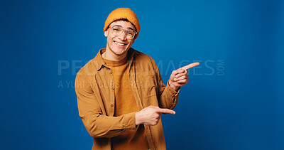 Buy stock photo Portrait, pointing and man in studio with smile, announcement and offer on blue background. Model, mockup space and happy person with hand gesture, promotion and opportunity with decision or choice
