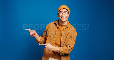 Buy stock photo Happy man, portrait and pointing with fashion in studio for advertising on a blue background. Male person, model or marketing with smile, gesture or selection for choice or option on mockup space