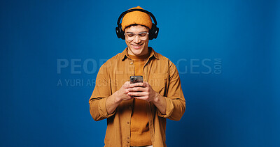 Buy stock photo Headphones, man and happy with phone in studio for music search, audio playlist or online video. Mockup space, person and smile with smartphone on blue background for listening to radio and sound app