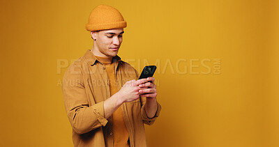 Buy stock photo Phone, smile and man in studio with networking, communication or texting on mobile app. Mockup space, technology and person with cellphone for chatting, contact or social media by yellow background.
