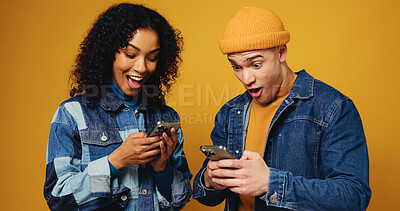Buy stock photo Phone, excited and couple in studio with networking, communication or chatting on mobile app. Happy, tech and man with woman on cellphone for contact on social media together by yellow background.