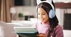 Happy, headphones and child on sofa on tablet for elearning, educational games and internet. Relax, weekend and girl on digital tech for watching videos, streaming movies and subscription in home