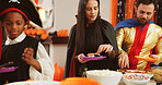 Halloween, parents or children with candy at party in home for holiday, costumes or celebration. Mom, dad or sweets for trick or treat tradition, fantasy dress up event or snacks with friends of kids