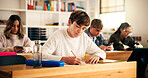 Boy, student and writing with books in classroom for higher education, learning or development. Male person, teenager and studying with textbooks in class for knowledge, assessment or test in school