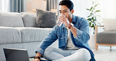 Buy stock photo Laptop, drinking water and man in home for remote work, reading report or news update on floor. Computer, thirsty freelancer and glass beverage in lounge, review headline and article for journalism